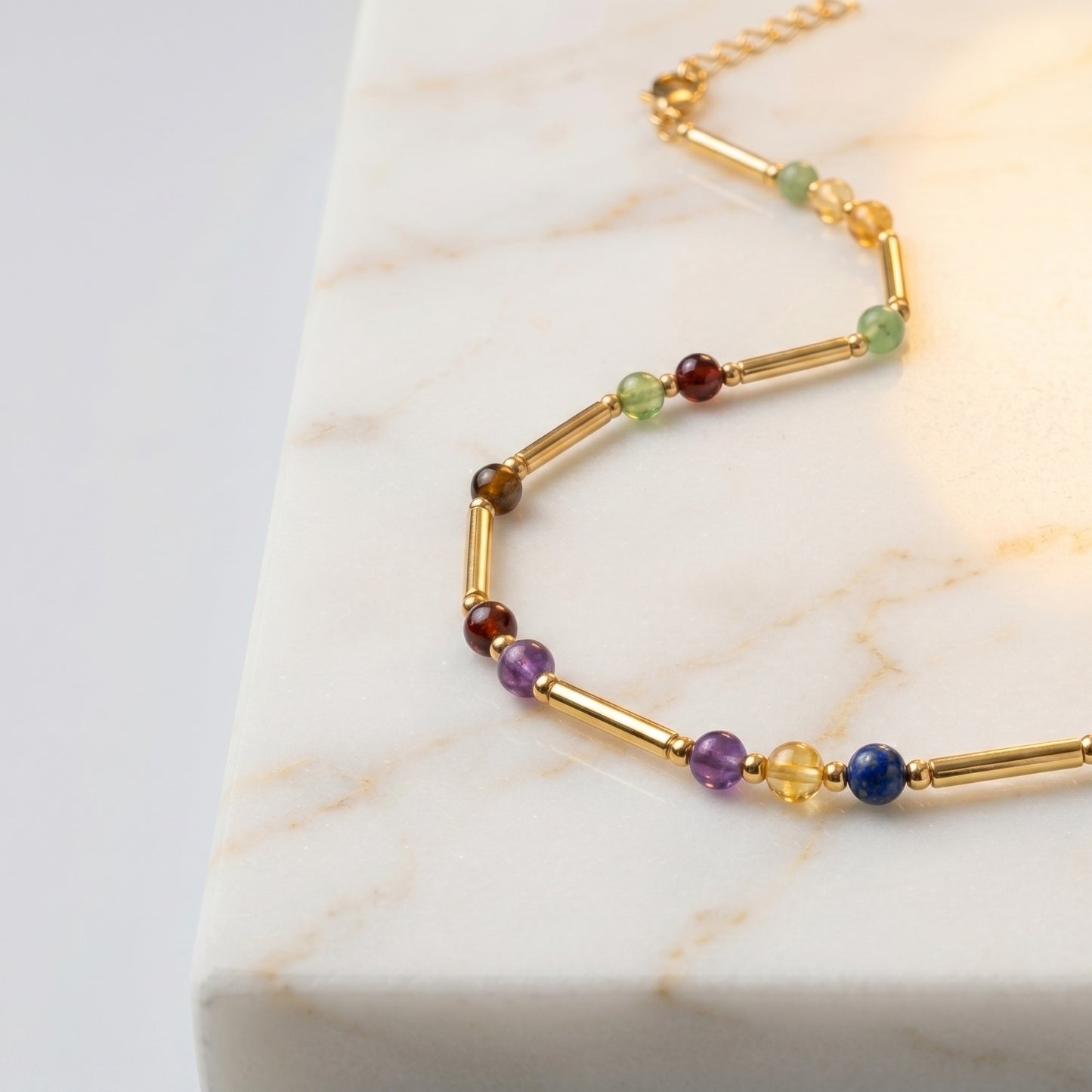 Close up of the gold necklace tubes and coloured stone markers on white marble