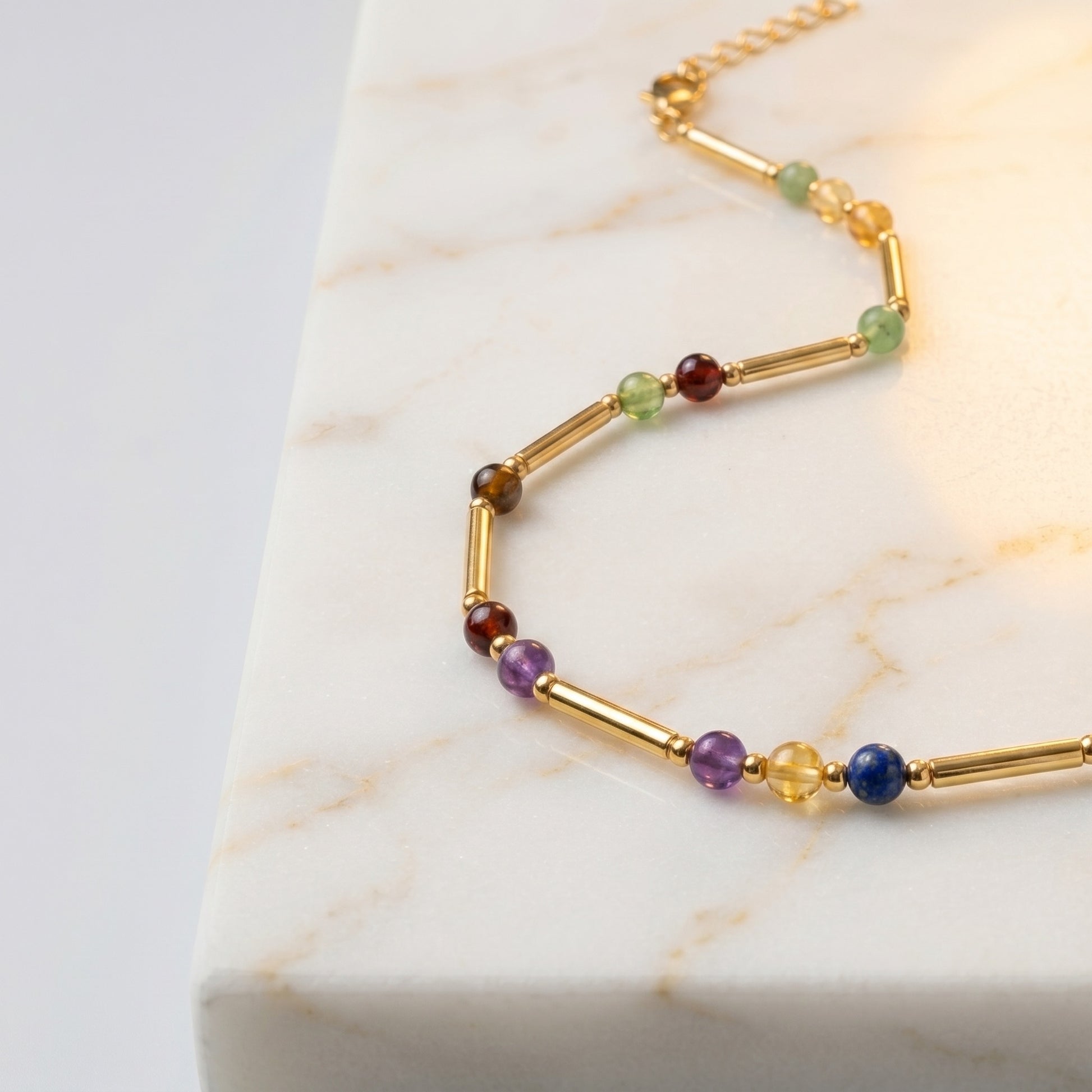 Close up of the gold necklace tubes and coloured stone markers on white marble