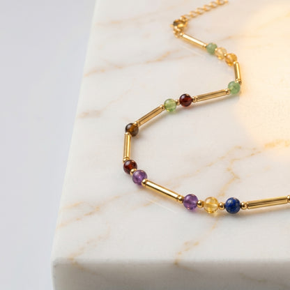 Close up of the gold necklace tubes and coloured stone markers on white marble