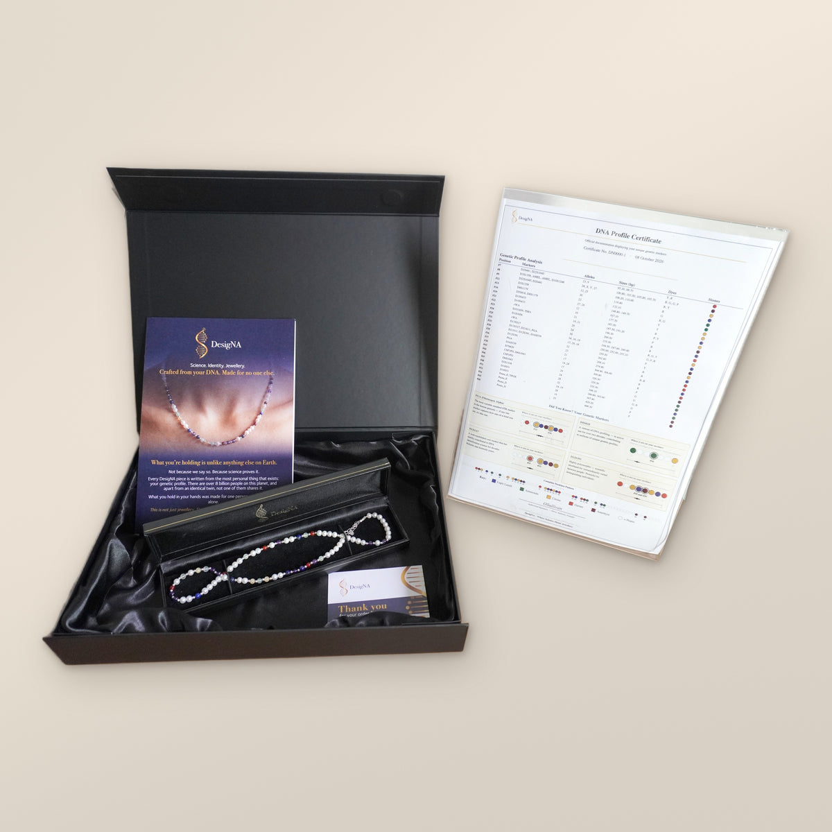 An open DesigNA box with a DNA profile necklace laid inside and its certificate of authenticity beside it