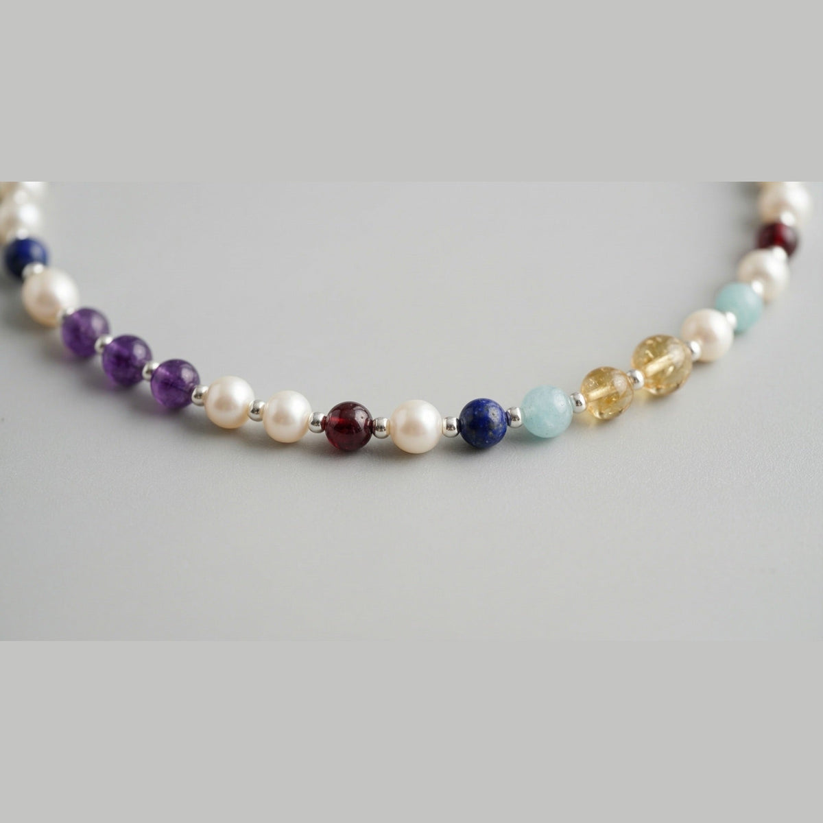 Close up of freshwater pearls, silver spheres and coloured stone markers on the pearl necklace