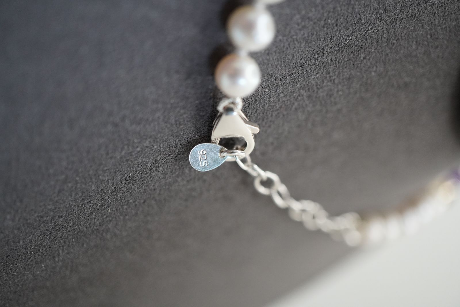 Macro of the DesigNA clasp, extender chain and stamped disc beside freshwater pearls