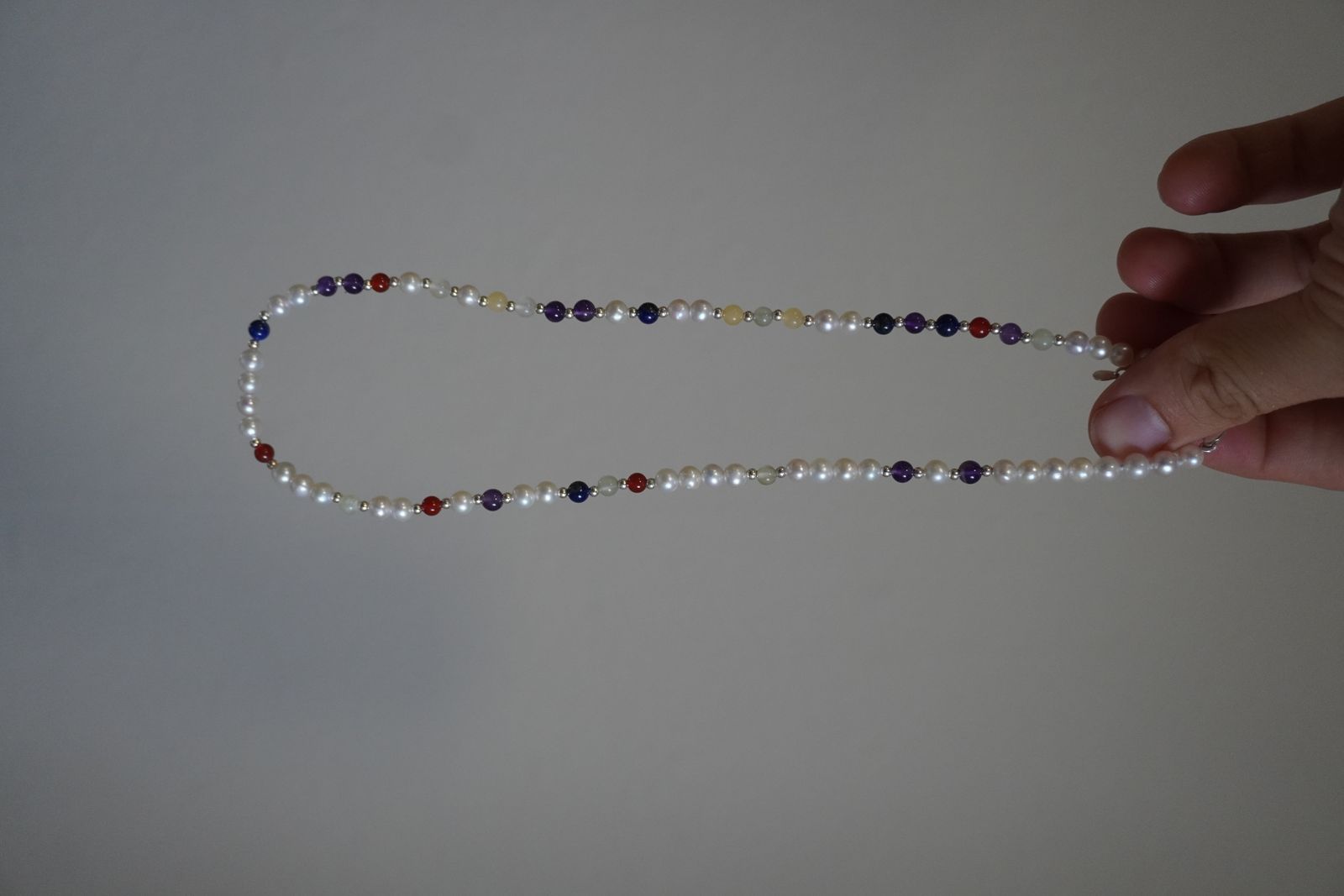 DesigNA pearl necklace held up by hand showing pearls and gemstone markers